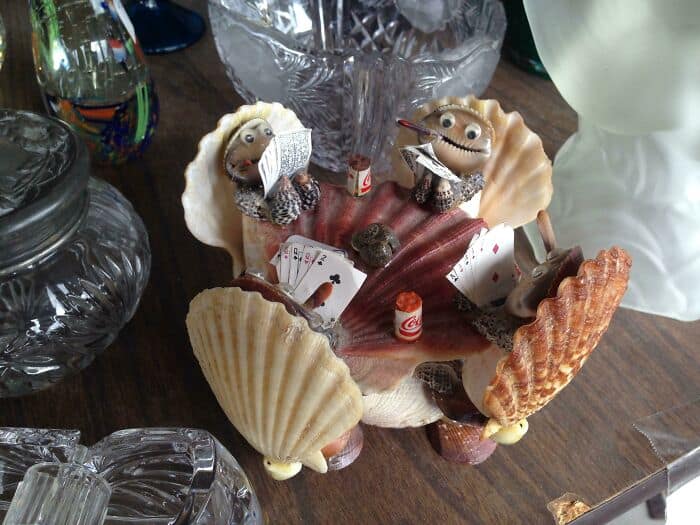 Shell-shaped decorative dish with two small figurines dressed as pirates, surrounded by seashells an.