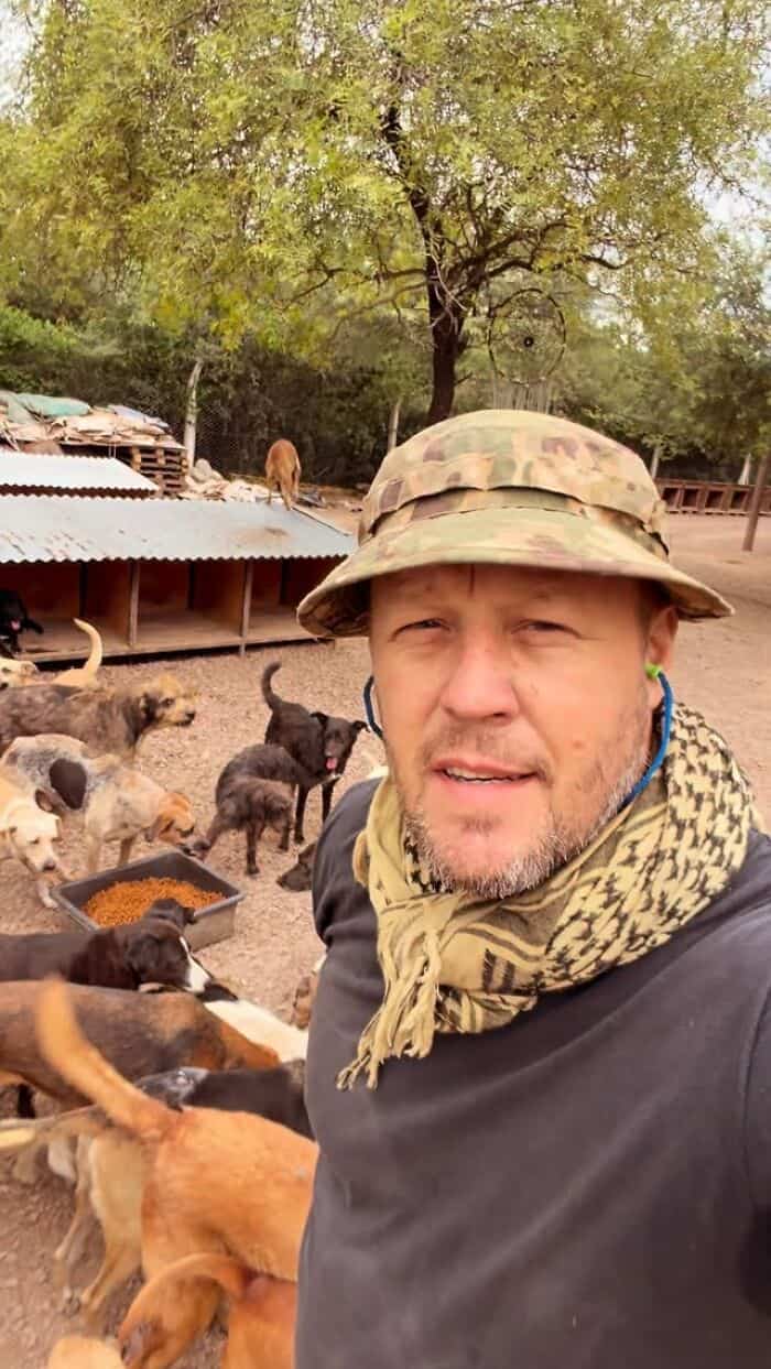 Man in camouflage hat with rescue dogs in outdoor shelter area.