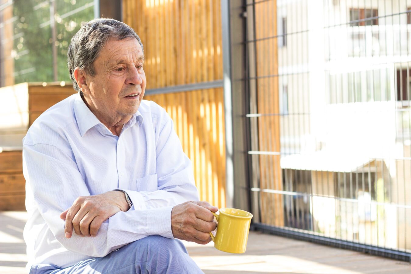 Older man sitting outdoors, holding a yellow mug, enjoying a peaceful moment.
