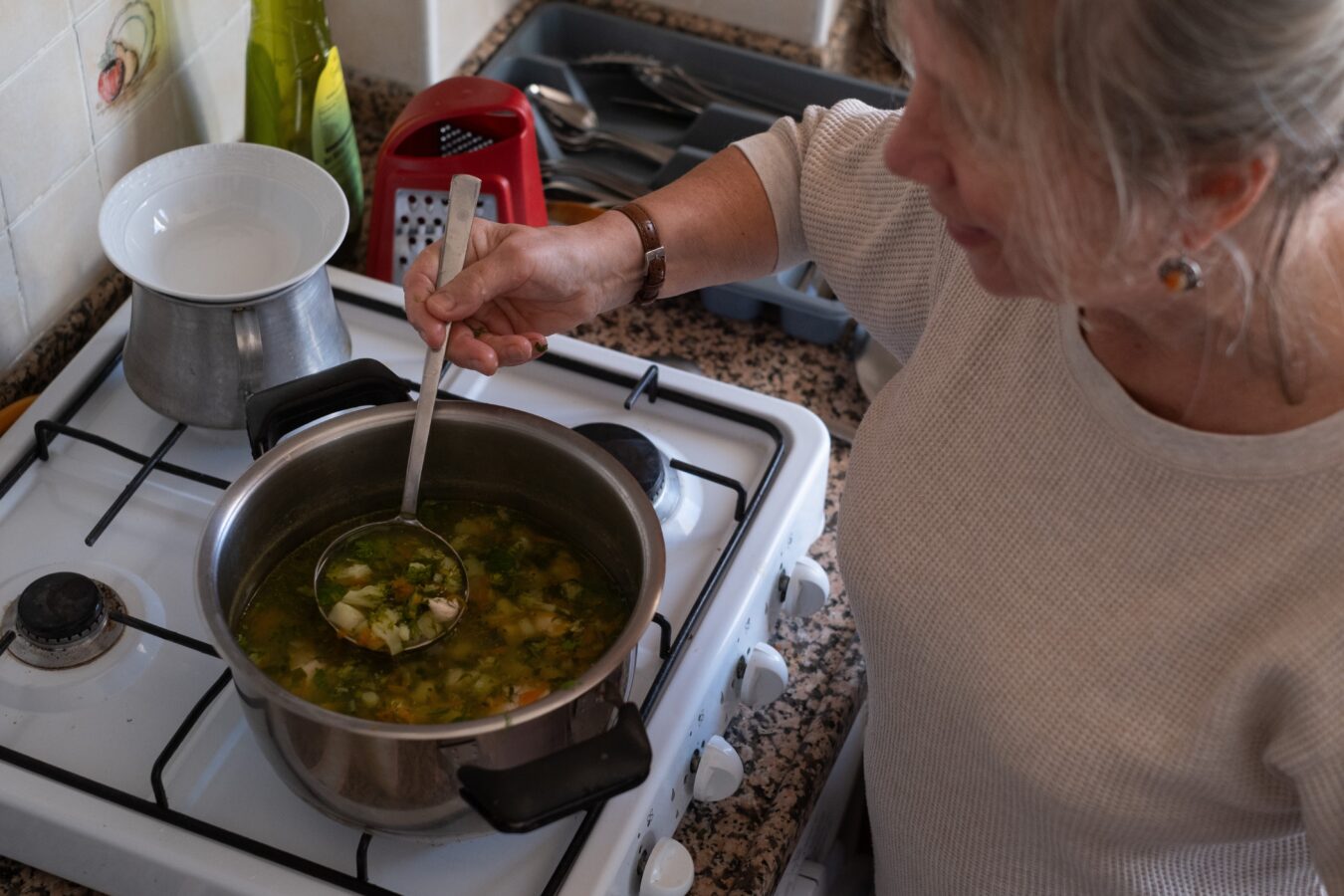 Woman cooking soup on stove in kitchen.