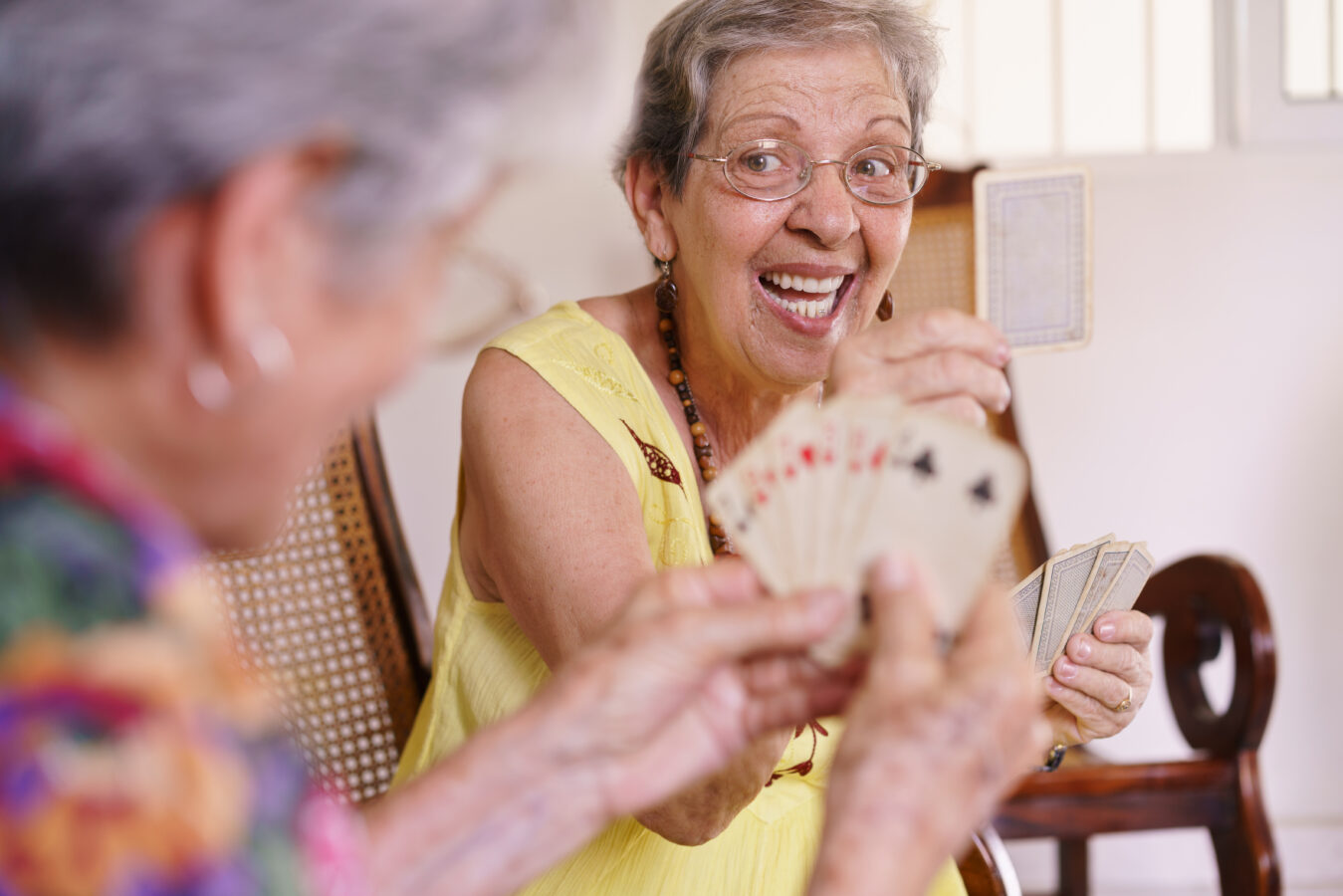 Happy elderly woman playing cards with a friend, smiling and enjoying the game.