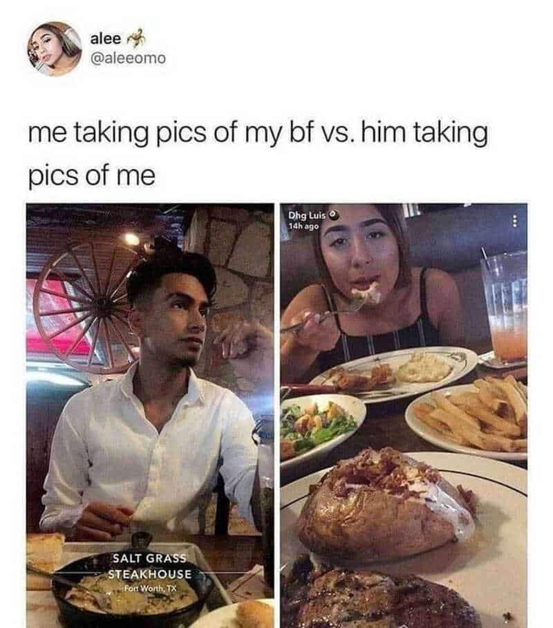 A woman taking a picture of her boyfriend, who is sitting at a restaurant table with food.