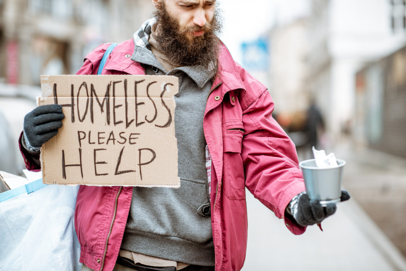 Homeless man holding a sign and a cup on the street.