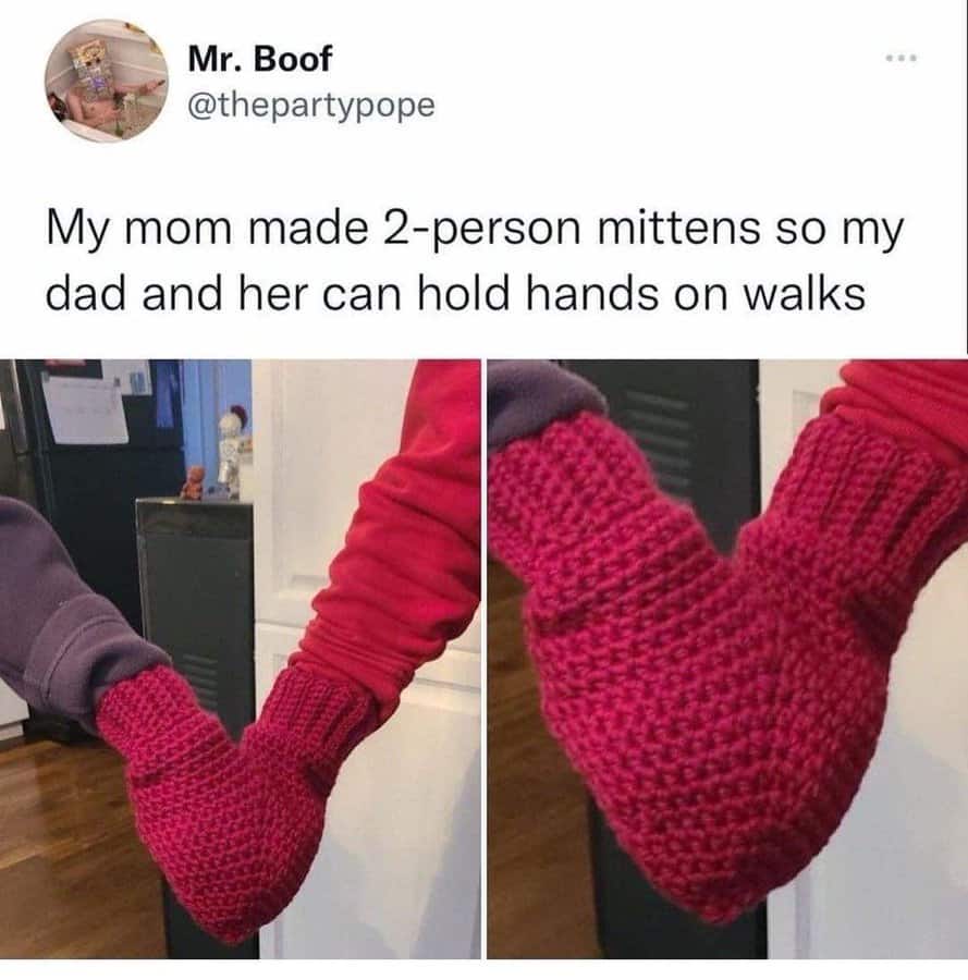 Two people holding hands, wearing matching red knitted mittens shaped like hearts.