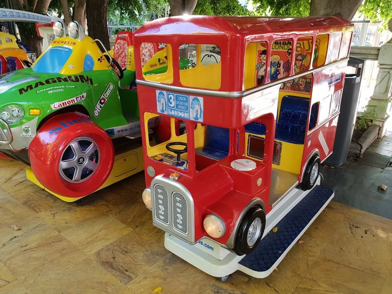 Colorful children's ride-on bus and car at the mall, with trees in the background.