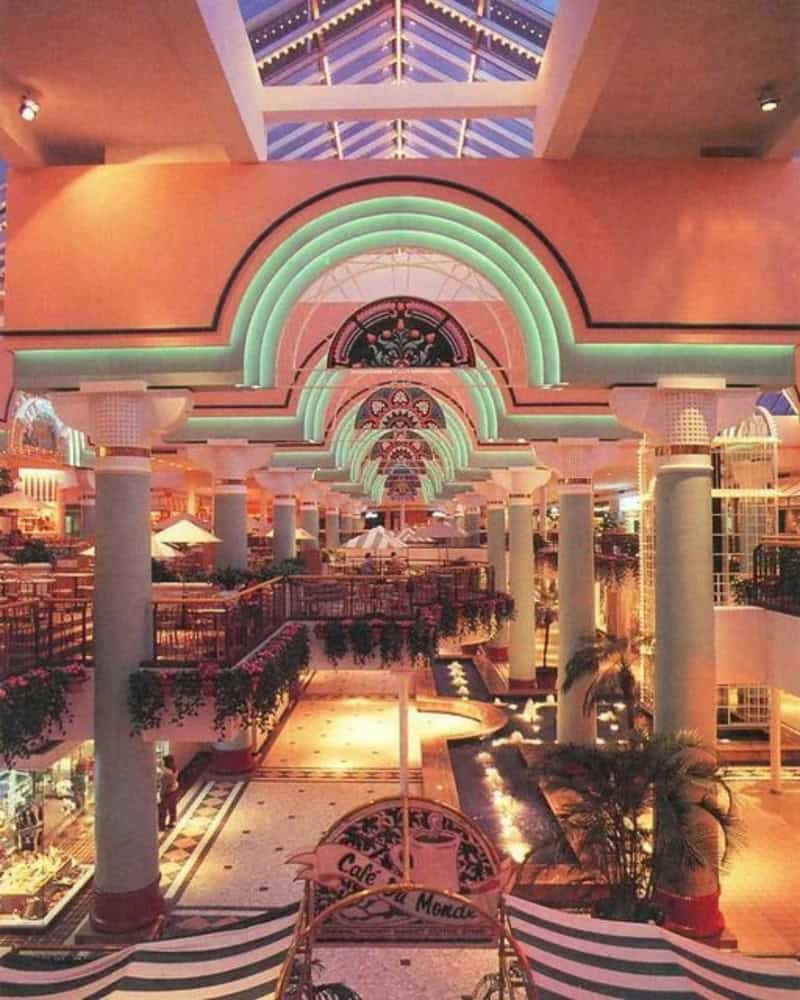 Colorful neon arches and columns inside a mall with plants and a water feature.