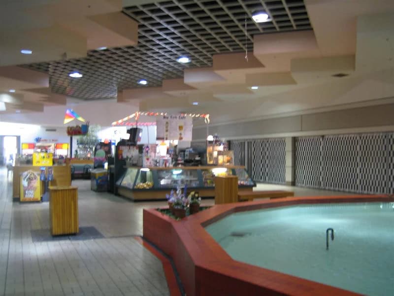 Empty mall food court with a hot tub in the foreground and arcade games in the background.