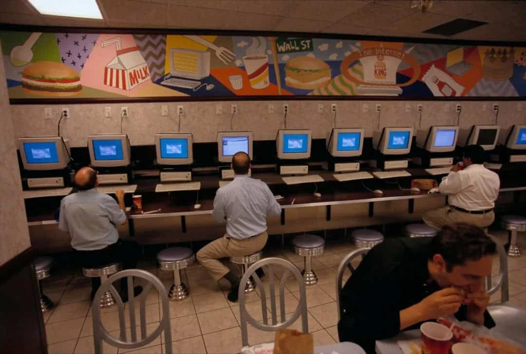 People using vintage internet cafe computers with a colorful mural above.