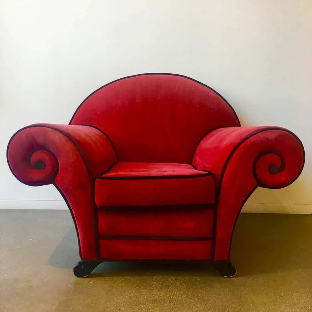 Red vintage armchair with curled armrests and black legs.