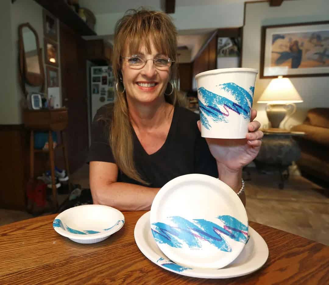 Woman smiling holding a paper cup with blue swirl design, with matching plates on table.