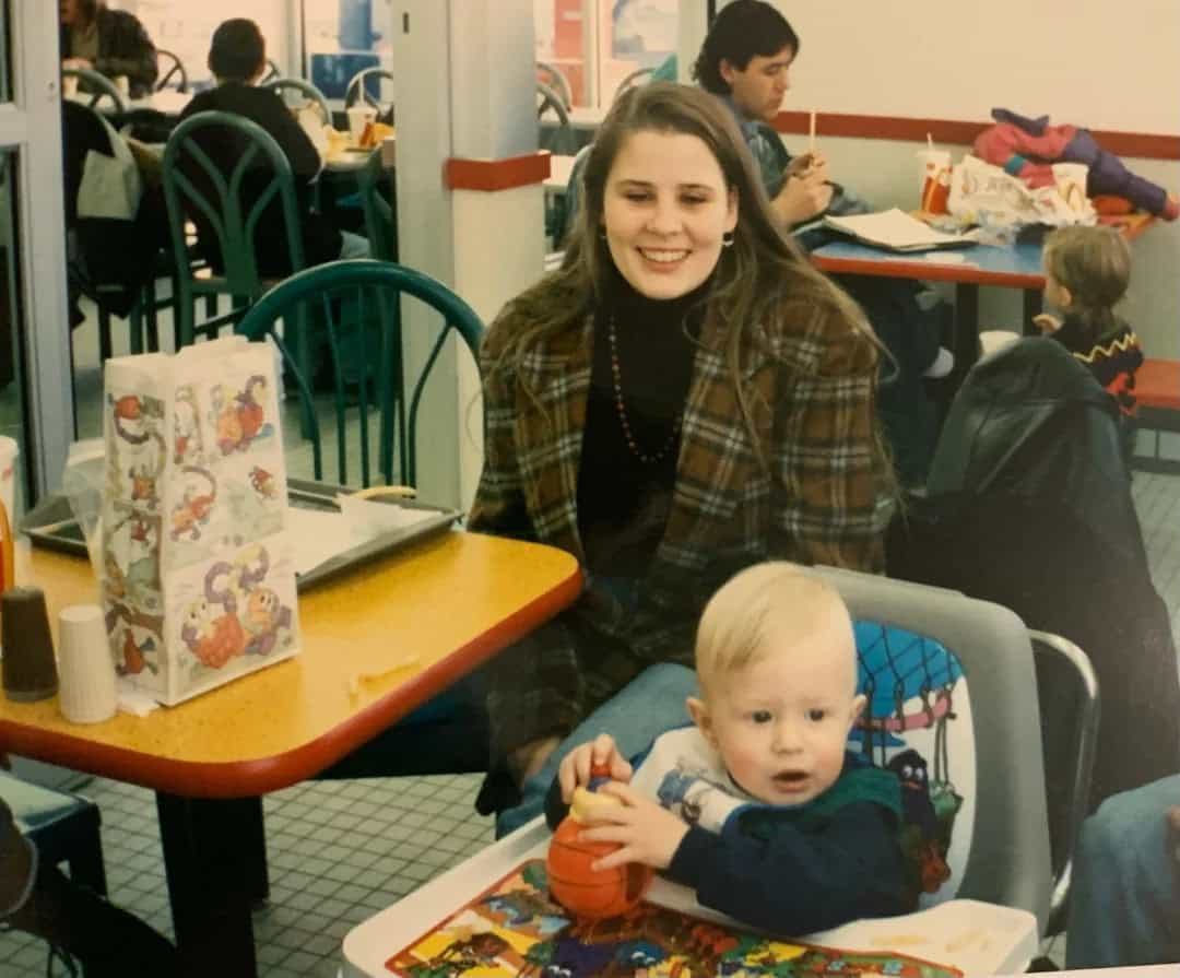 Young woman with long brown hair smiling at a toddler in a high chair at a restaurant.