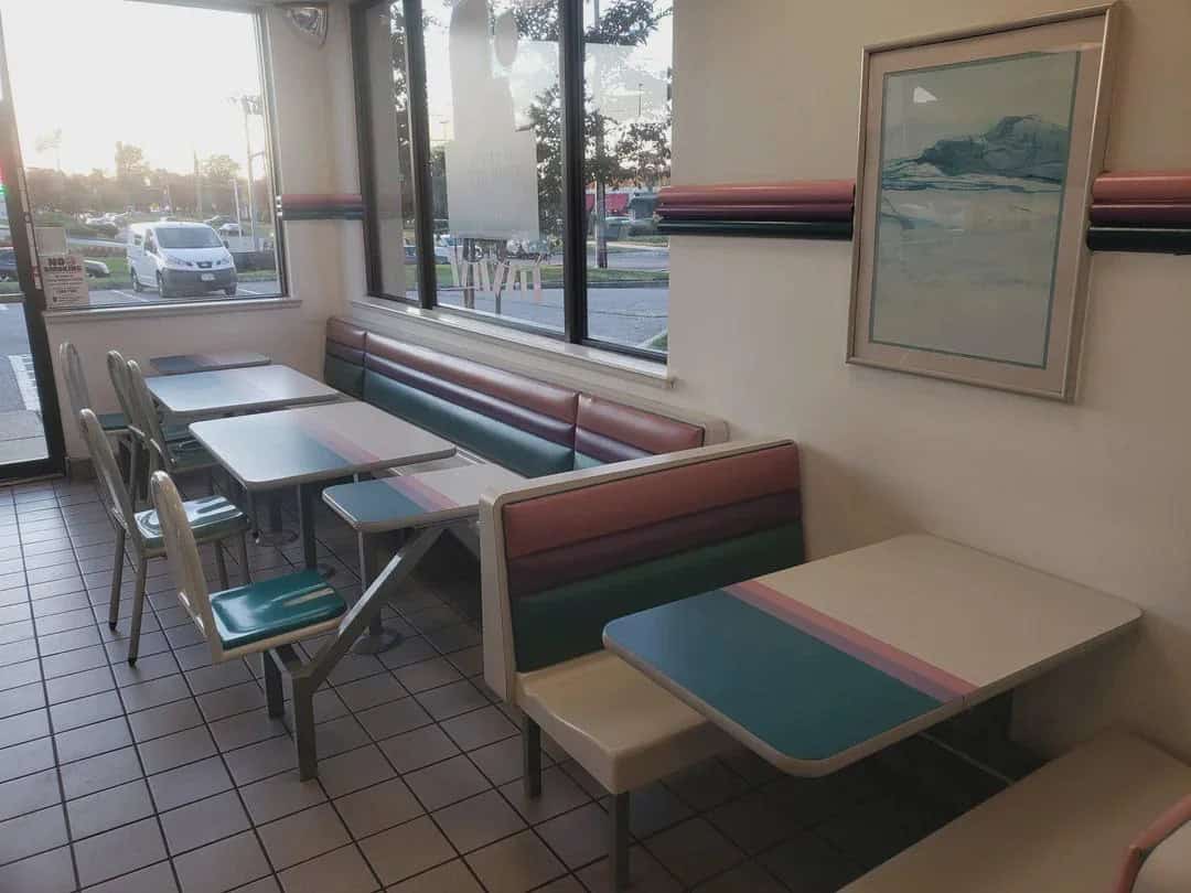 Empty retro diner booth with pastel-colored tables and chairs, sunlight outside.