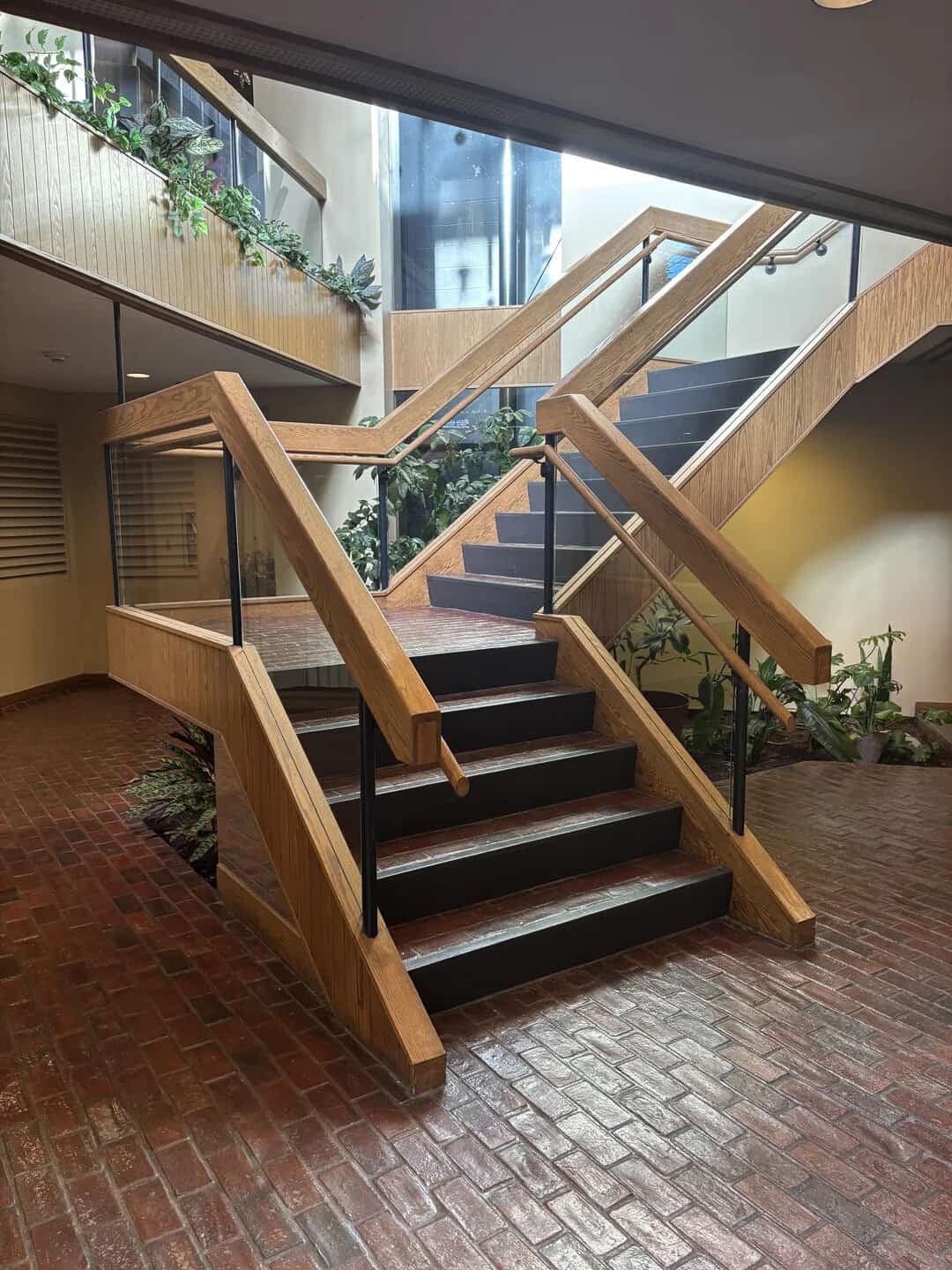 Modern wooden staircase with black steps and glass railing in a contemporary building.