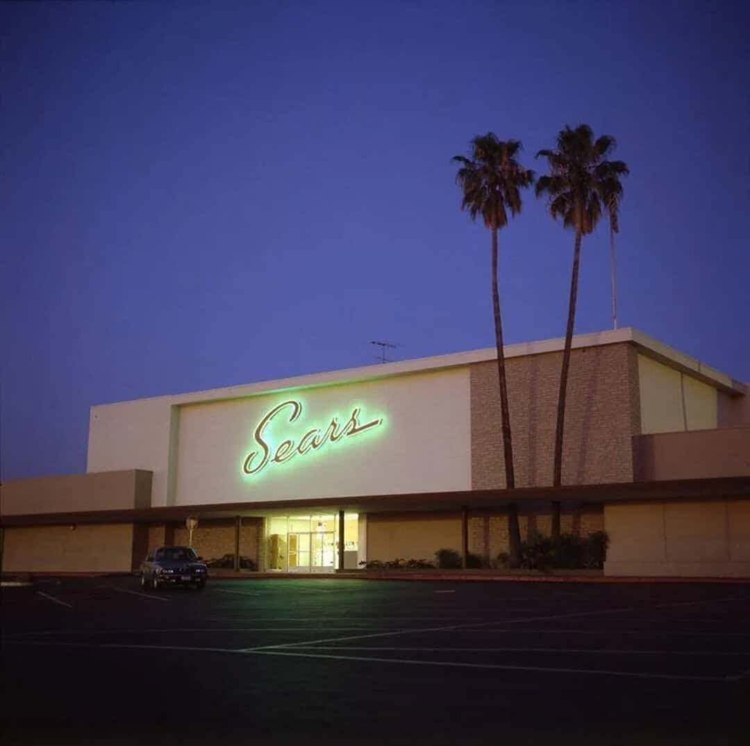 Sears store with neon sign and palm trees at dusk, 90s nostalgia.