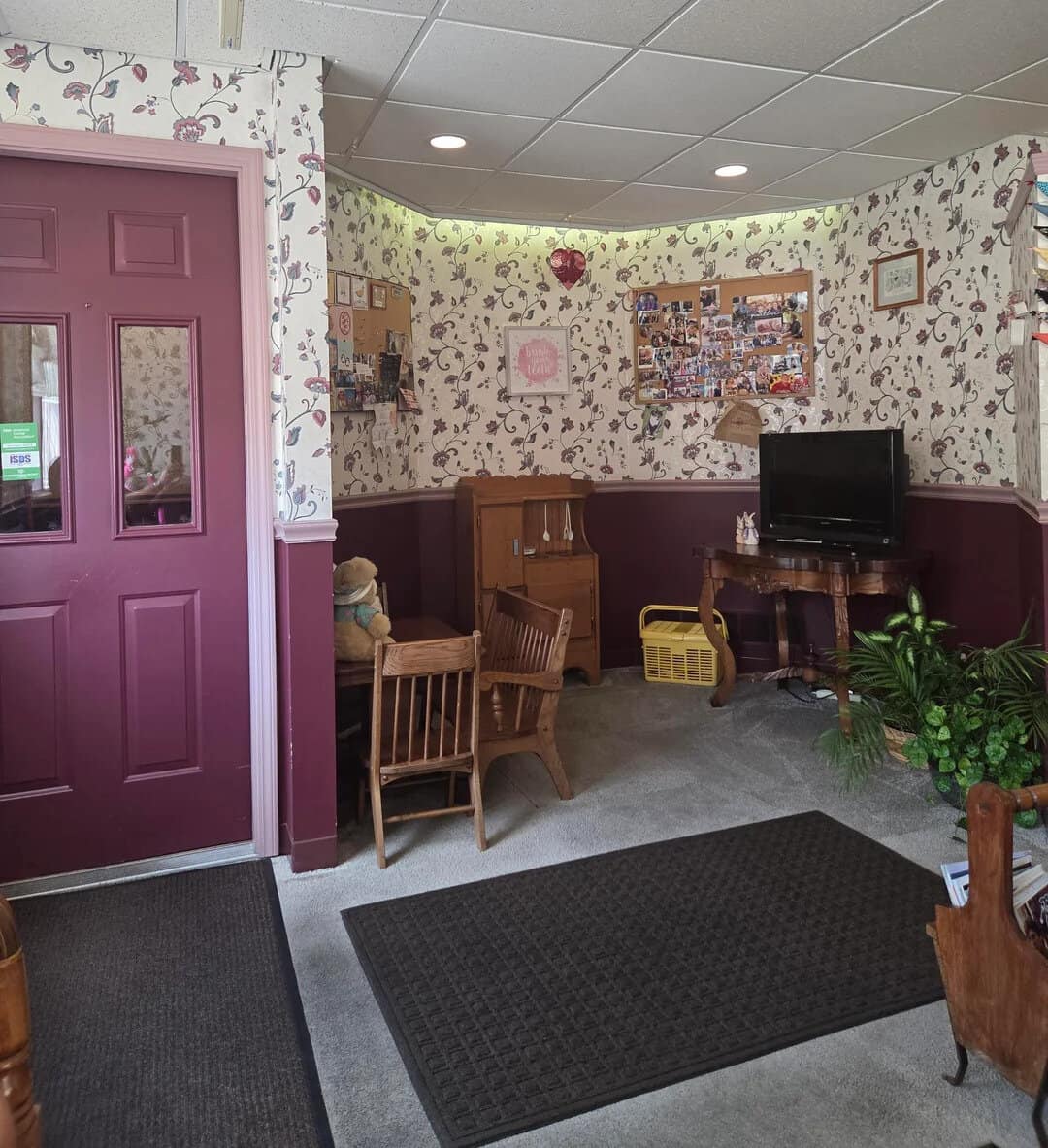 Cozy waiting area with floral wallpaper, wooden furniture, and a TV.