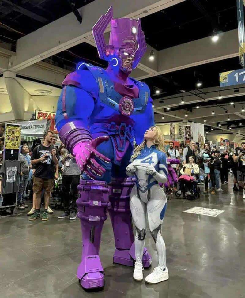 Large purple and blue Thanos statue with a woman in a white and blue costume at a convention.