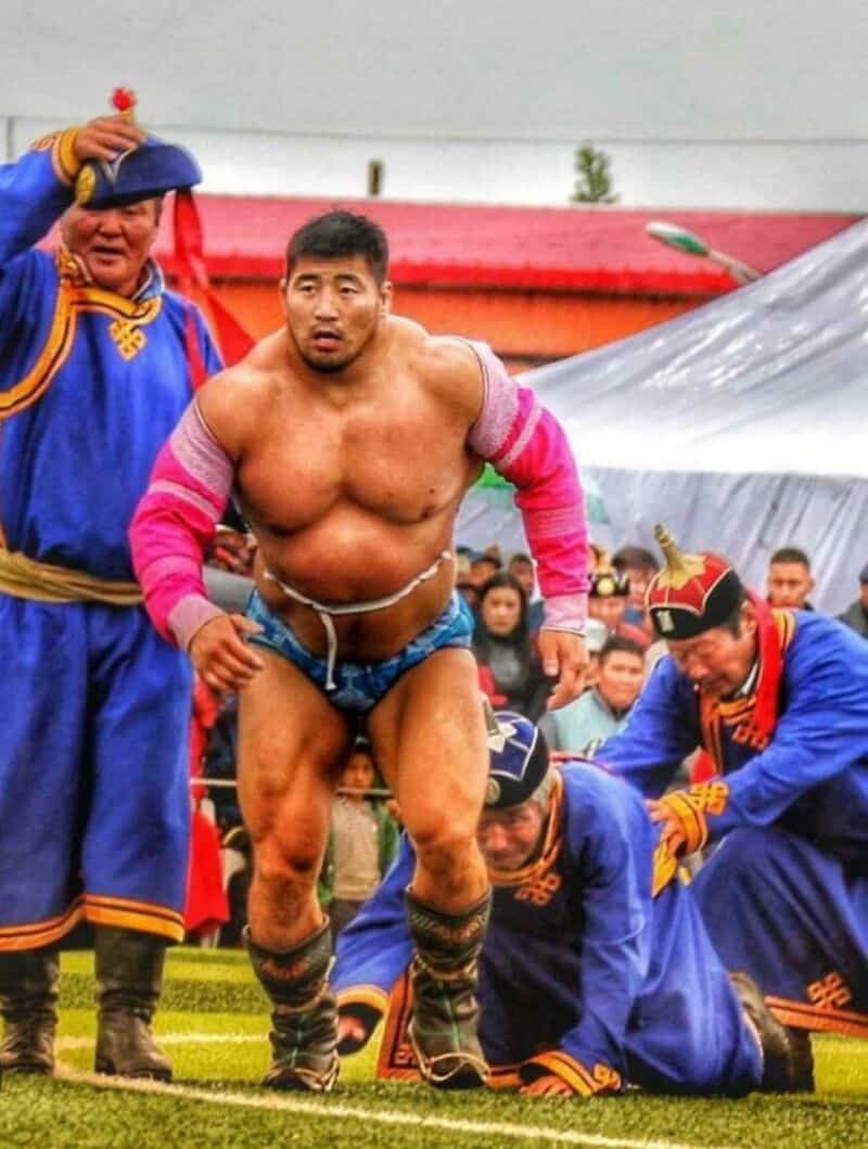 Sumo wrestler in blue and pink attire with officials around him during a match.