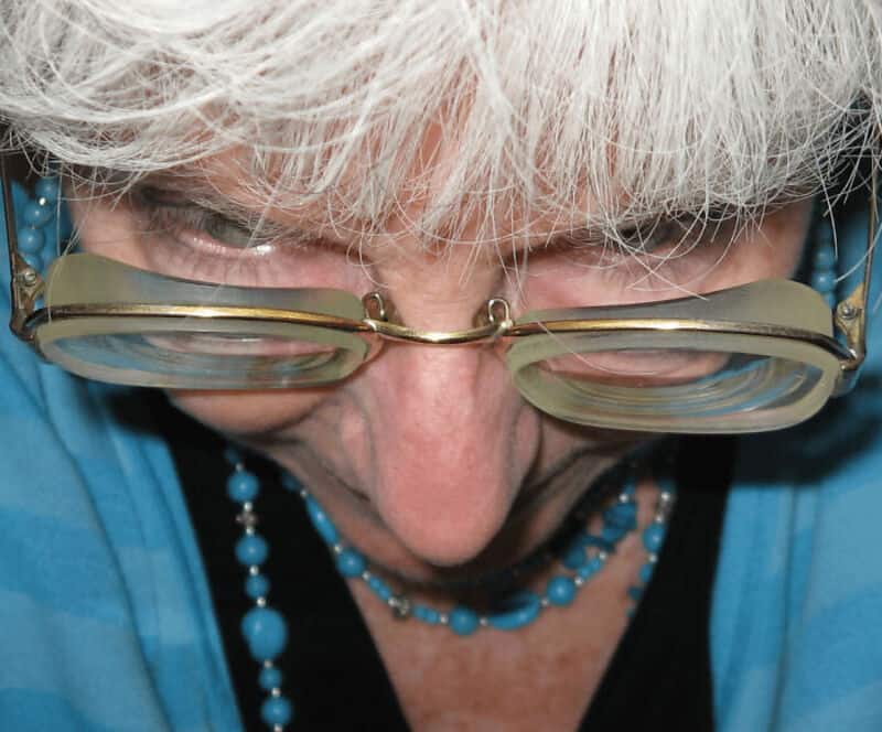 Close-up of an elderly woman with glasses and white hair, looking down.