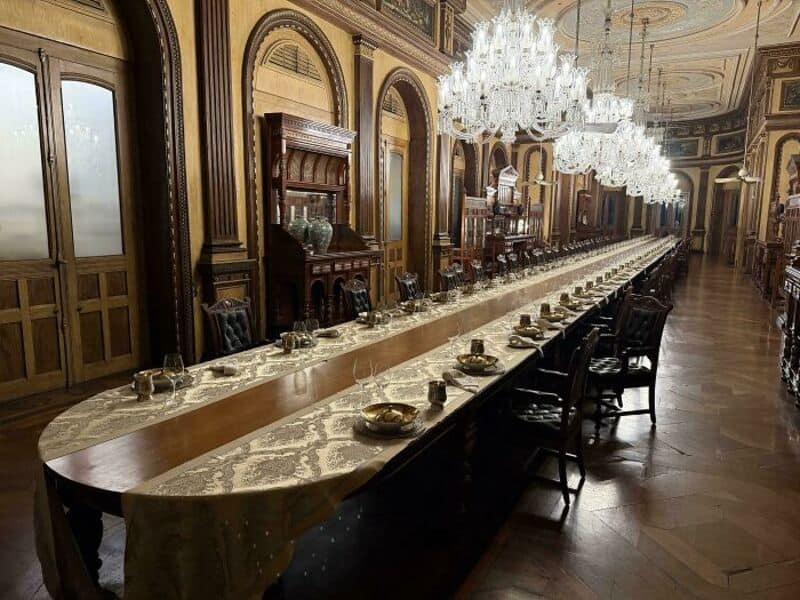 Long luxurious dining hall with chandeliers and ornate woodwork.