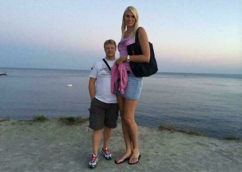 A tall woman and a shorter boy standing on a beach at sunset.