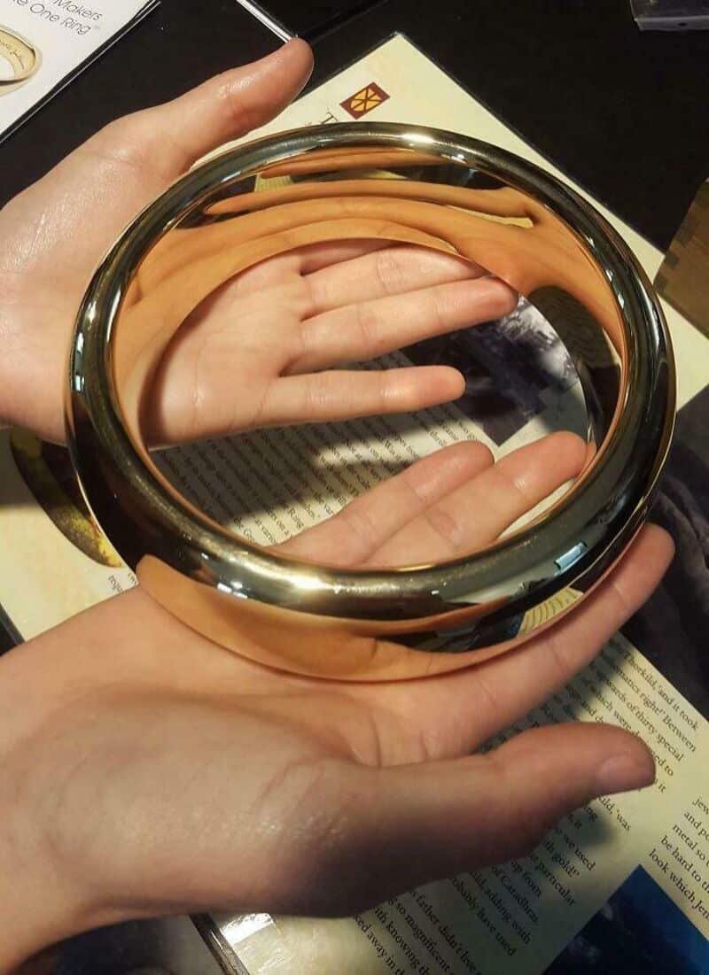 A hand holding a large, round, reflective mirror with a gold rim, showing a reflection of another, a.