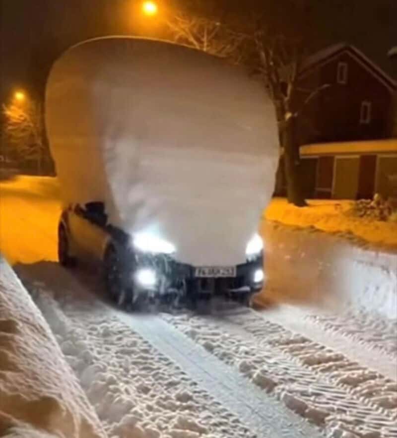 Car with a huge snow pile on top, blocking the view of the vehicle's roof.