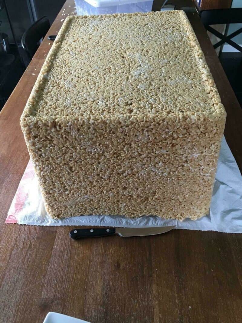 Large cube covered in small beige particles on a wooden table.