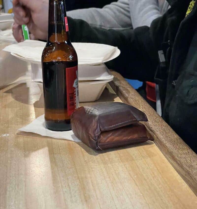 A beer bottle and a brown leather wallet on a wooden table.