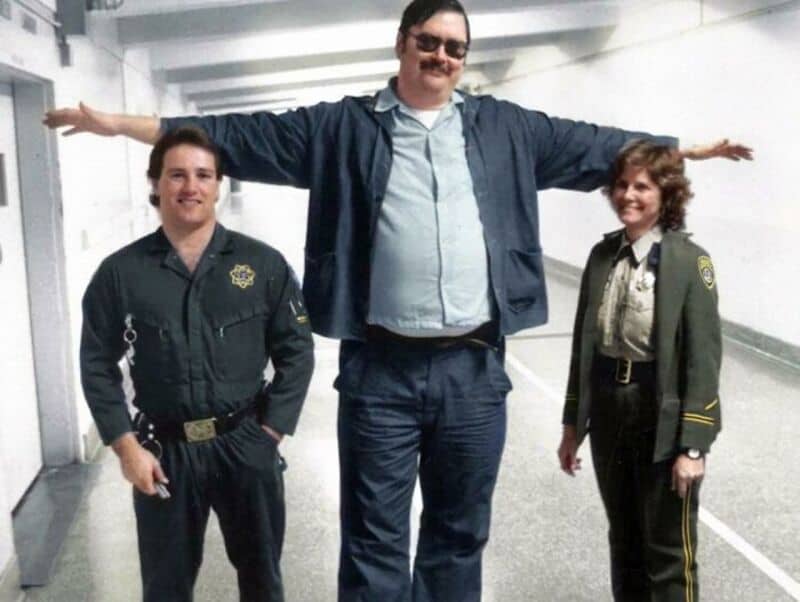 Three people, two women in police uniforms and one man with arms outstretched, in a corridor.
