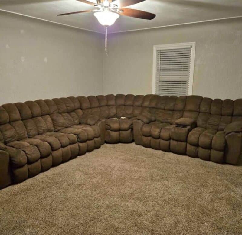 Large brown sectional sofa in a living room with a ceiling fan and window.
