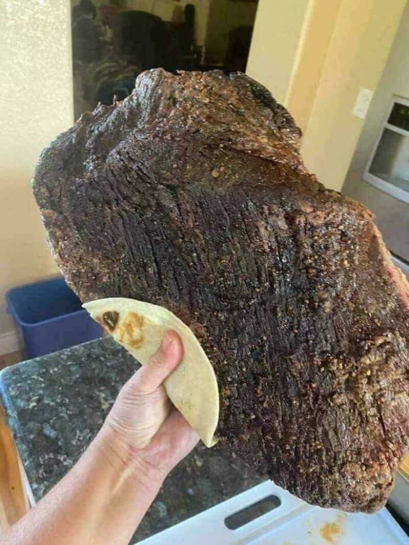 Huge burnt steak held with a tortilla in a kitchen setting.