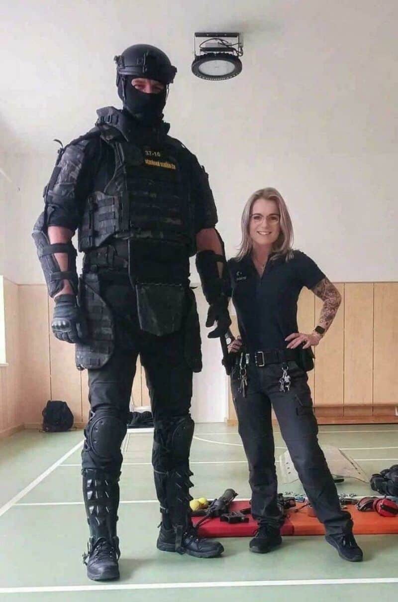 Large armed officer and smiling woman in a gym, comparison of size.