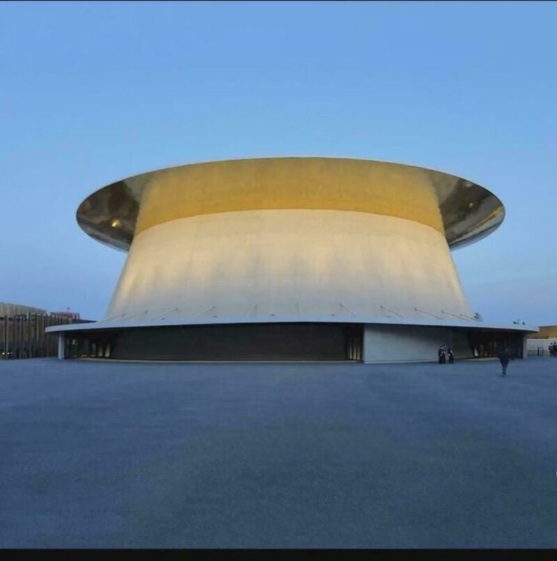 Unique modern building with a curved, gold and white exterior under a blue sky.