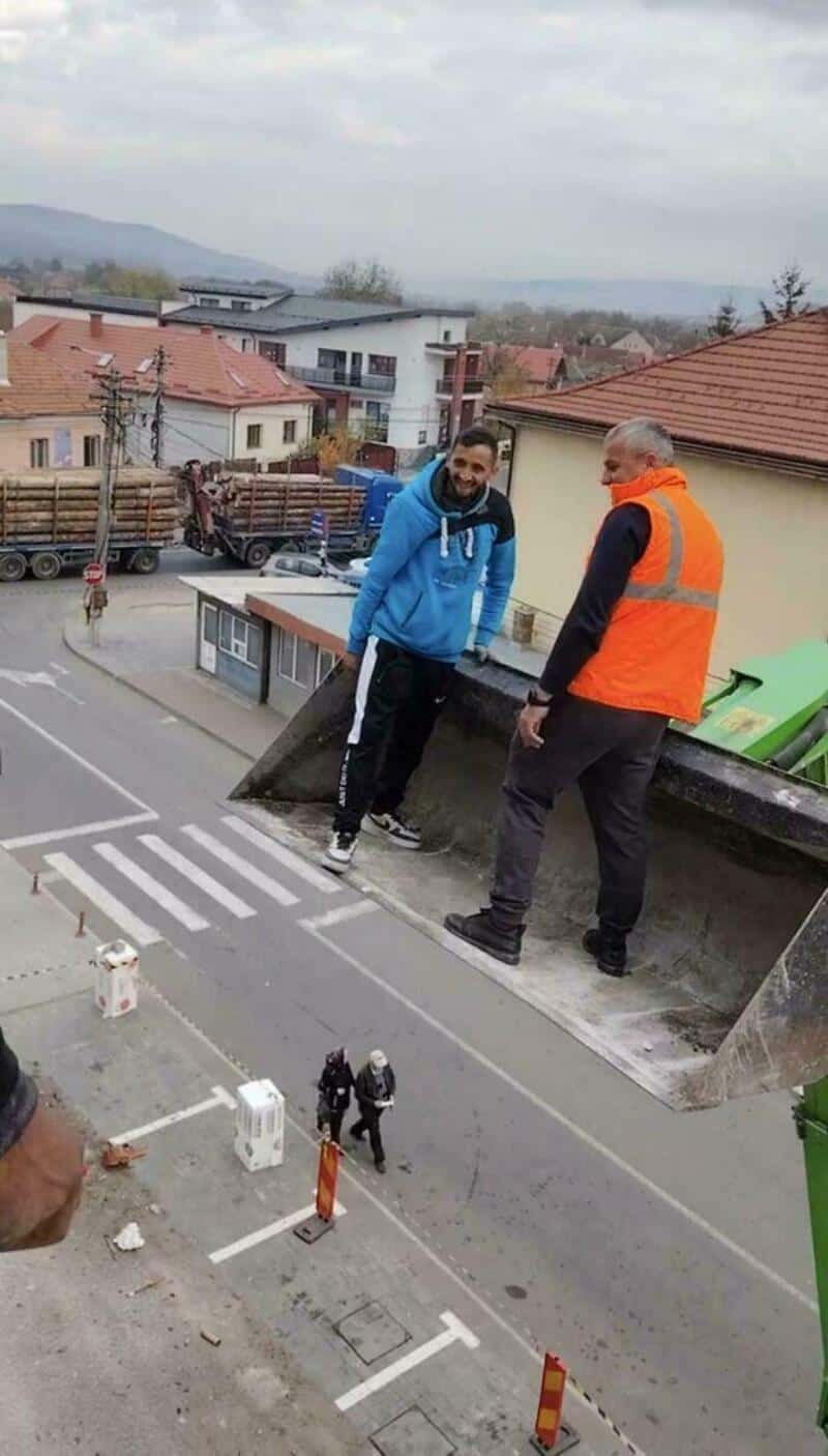 Two men on a rooftop with a miniature street scene below, confusing perspective.