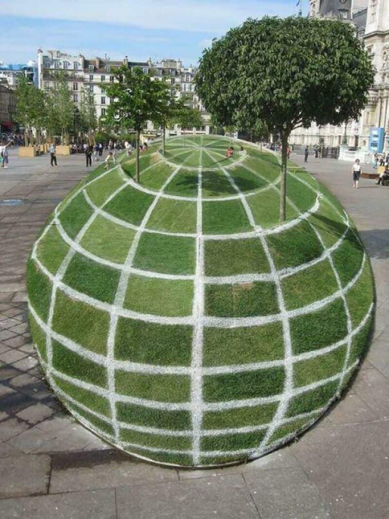 Spherical grass installation with grid pattern and trees on top in a city square.