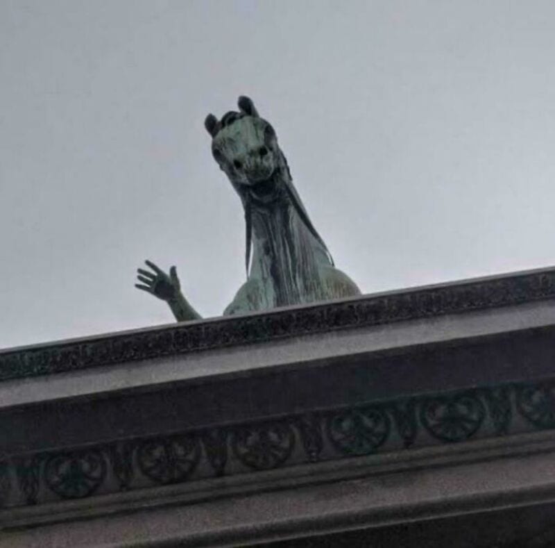 A giraffe sculpture peeking over a building with a waving hand.