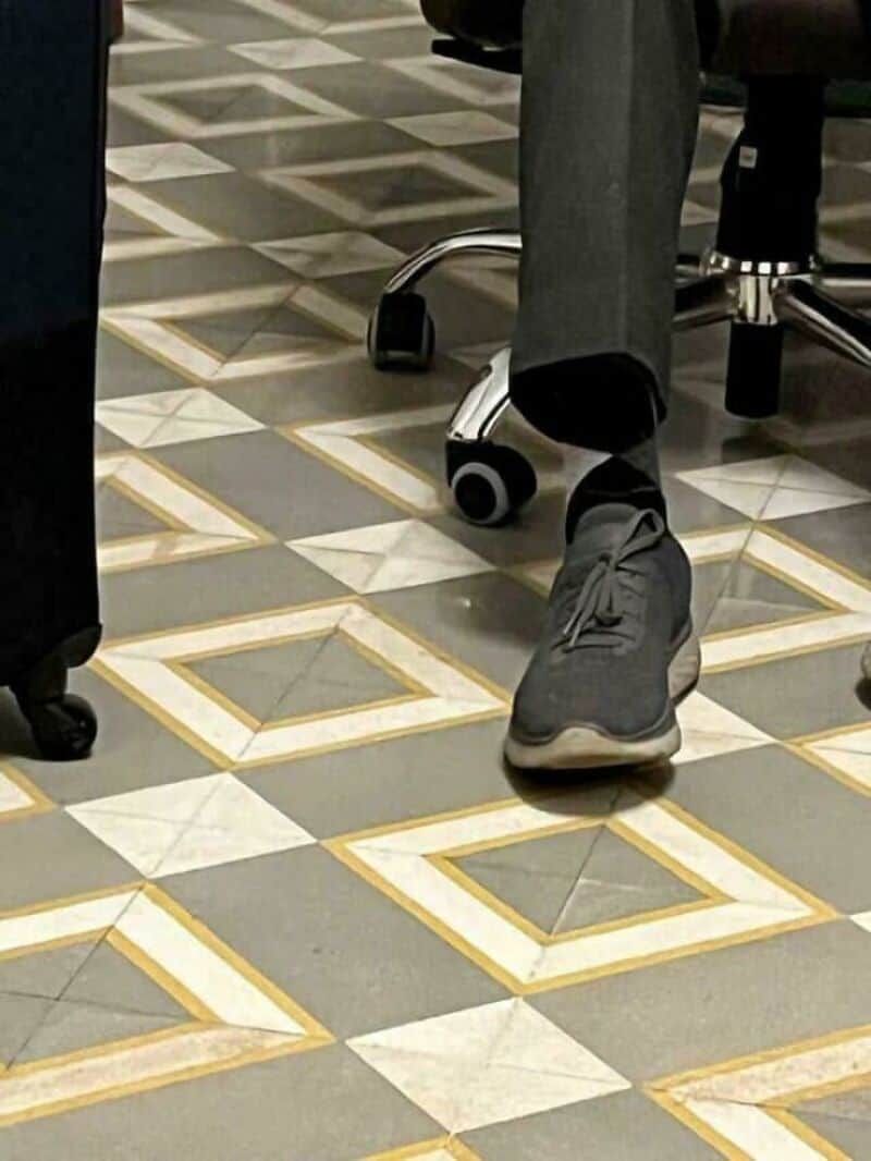 Person sitting on a chair with one foot on the patterned floor.