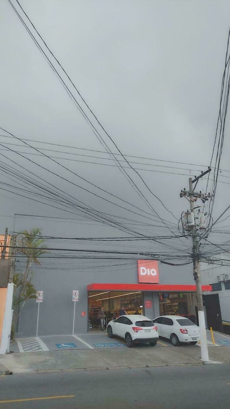 Power lines and a store with a red sign under a cloudy sky.