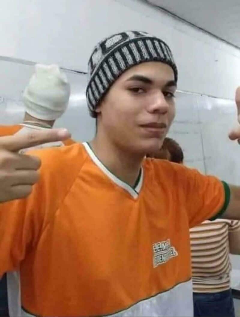 Young man in orange shirt and striped beanie holding ice cream with two fingers.