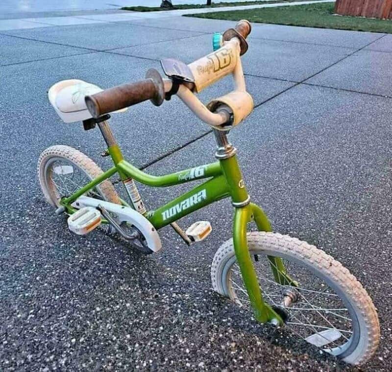 Child's green bicycle with rusted handlebars on wet pavement.