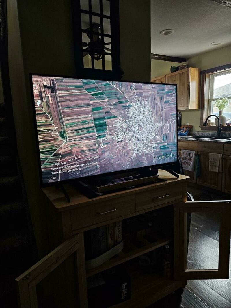 TV screen showing a distorted, pixelated aerial view of farmland and a town.