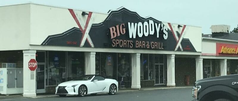 Big Woody's Sports Bar & Grill sign with a white sports car parked in front.