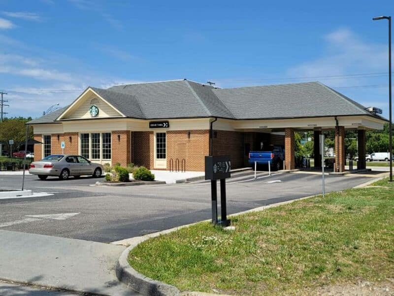 A brick building with a clock, parking lot, and a covered drive-thru area.