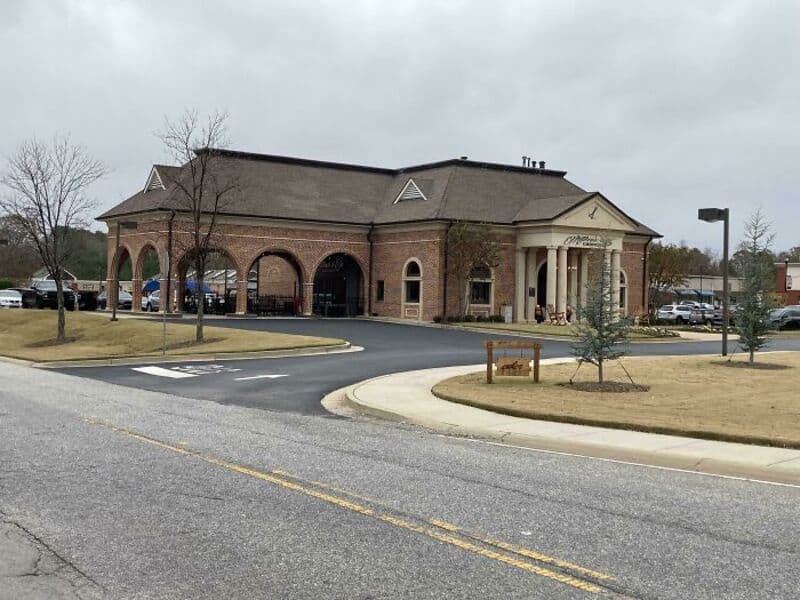 Brick building with arches and a small front porch, parking lot nearby.