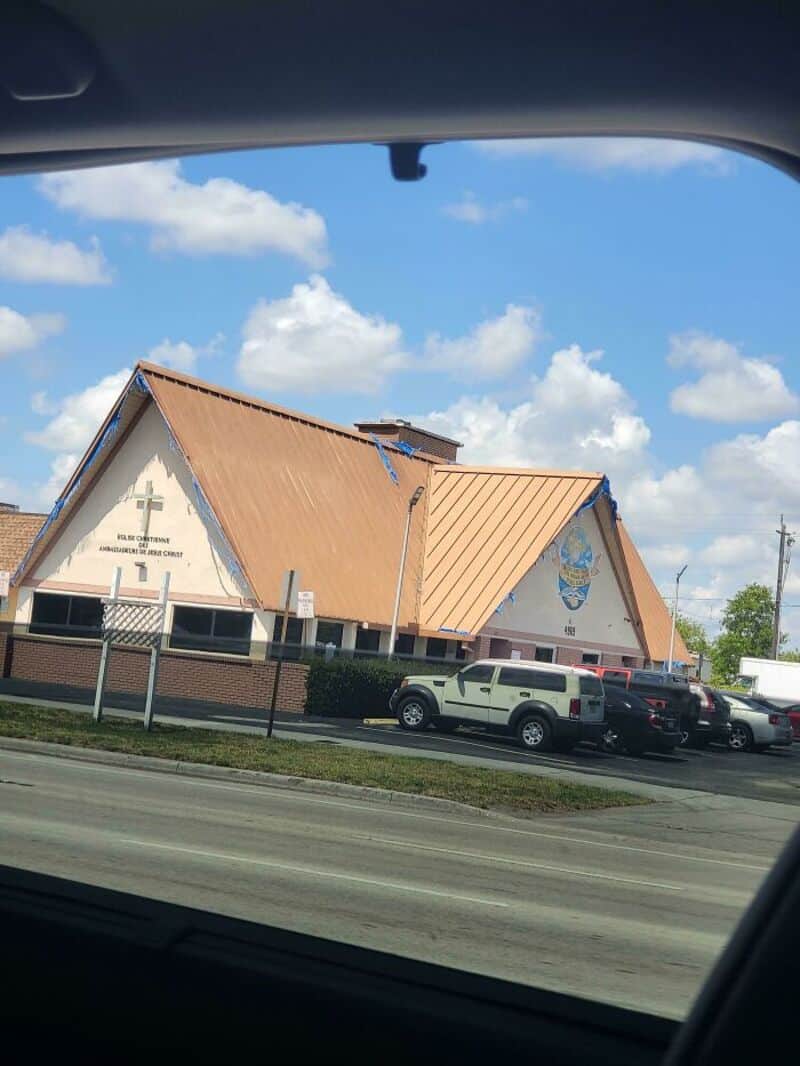 Converted building with a sloped roof and religious symbols, parked cars in front.