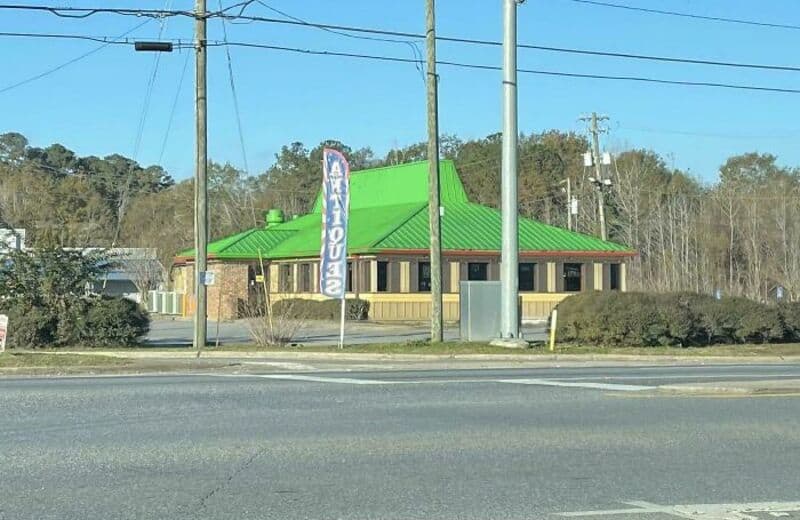 Building with a green roof and a sign that says 'AQUARIUM' in front of power lines.