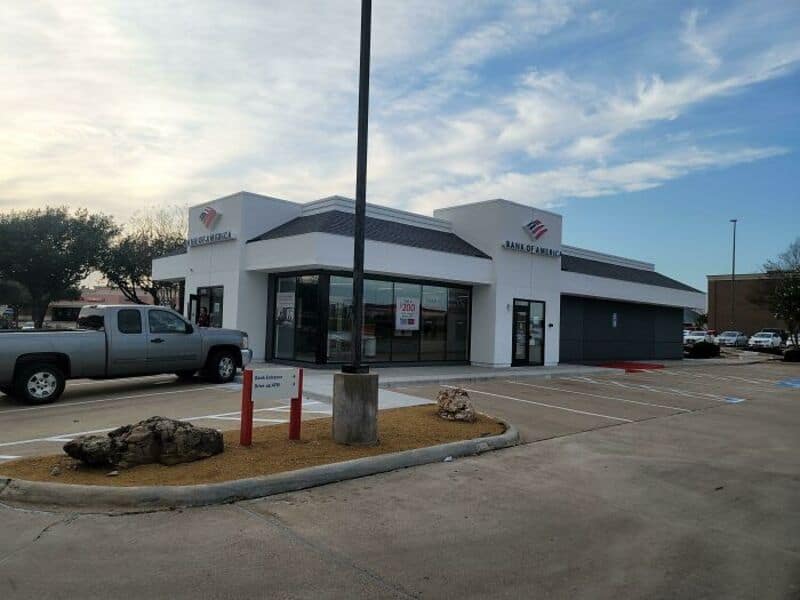 Bank of America branch in a shopping center with parking lot and rocks in front.