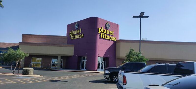 Planet Fitness gym in a shopping center with parking lot and cars.
