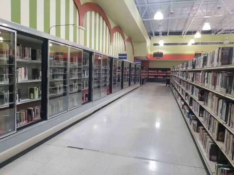 Empty library aisle with bookshelves and glass-fronted refrigerators.