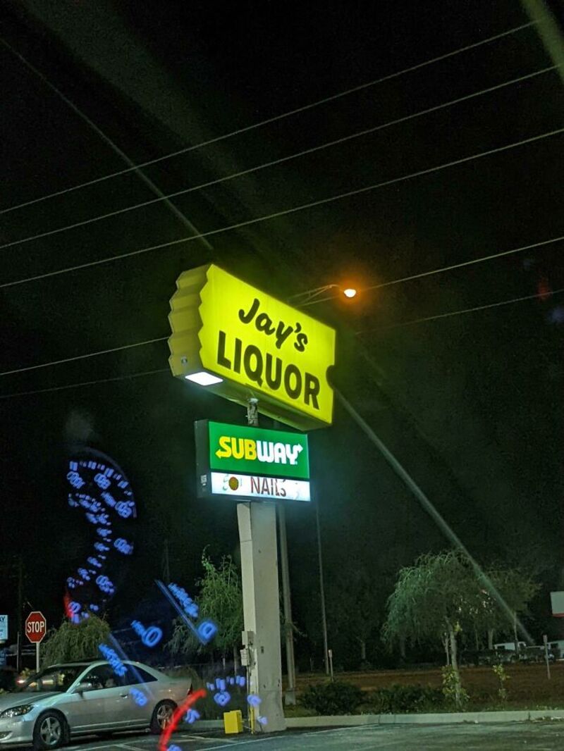 Jay's Liquor sign with Subway and Nails signs below at night.